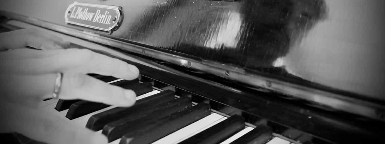 An artistically grainy, black and white photo of the skillful
            hands of a musician, hovering above a piano keyboard, just about to engage in playing a moving piece